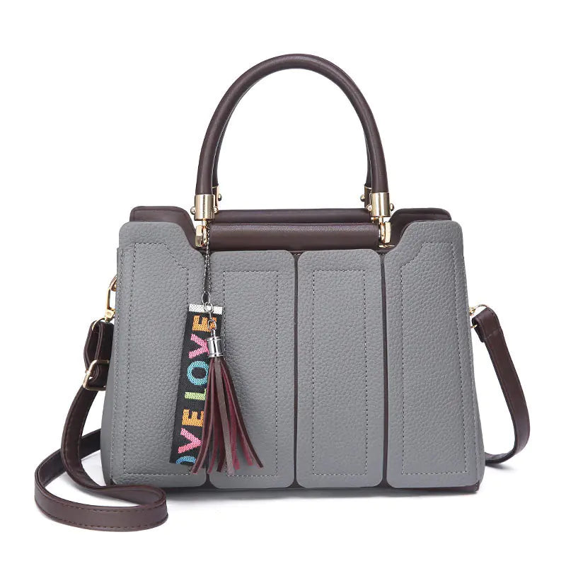 Grey shoulder tote bag with brown top handle and side strap, tasseled keychain, four panels