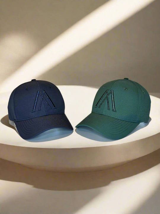 Zwei Baseballkappen auf Podest: dunkelblau mit A-Logo, grün daneben