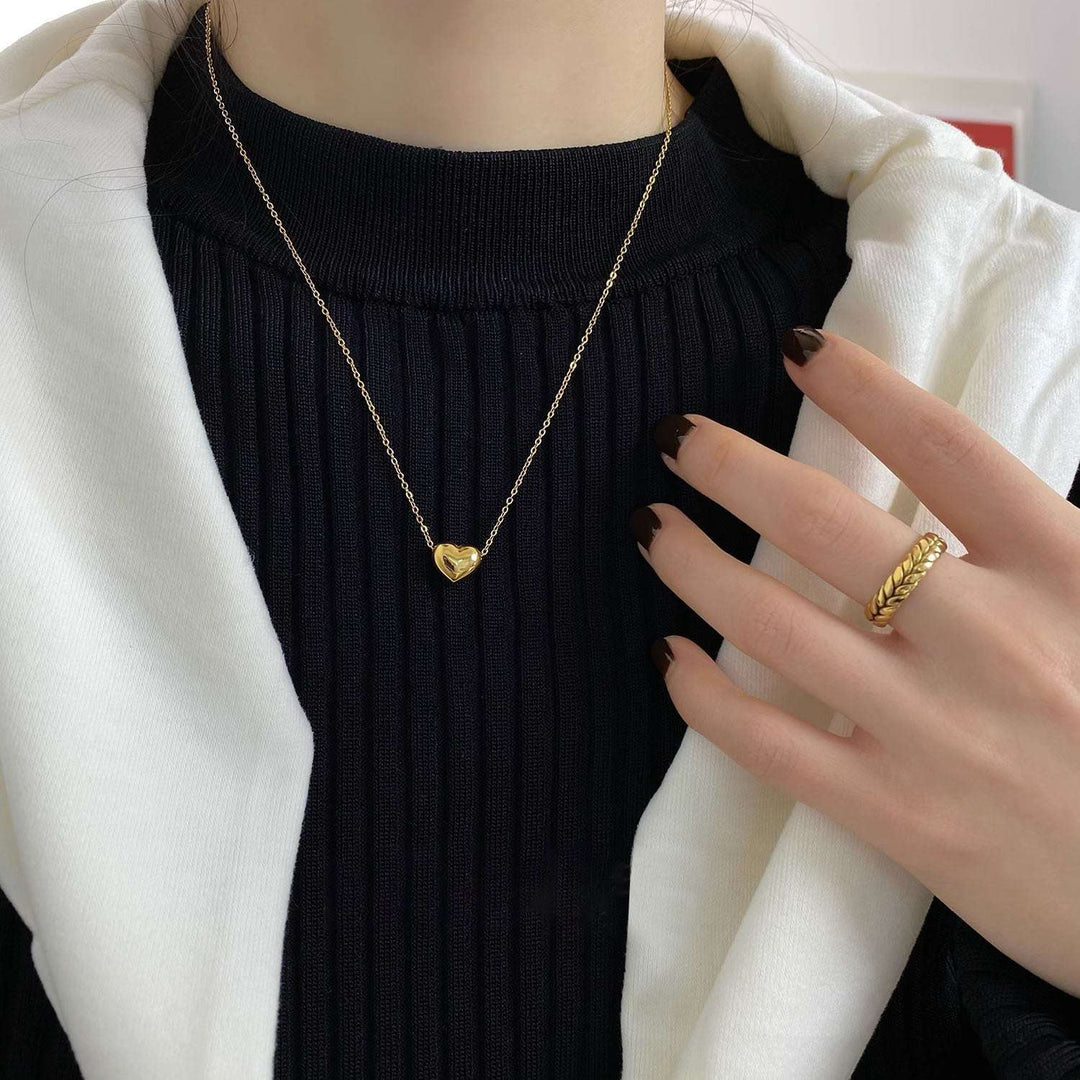Gold heart pendant on a fine chain necklace, worn with a knit neckline