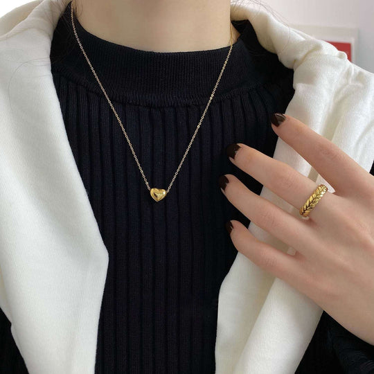 Gold heart pendant on a fine chain necklace, worn with a knit neckline