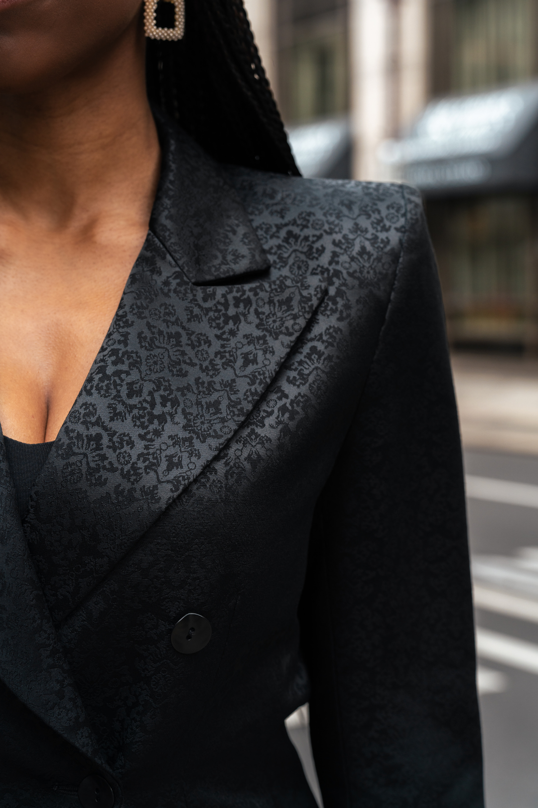 Black blazer close-up: notch lapel, textured pattern panel, dark button placket