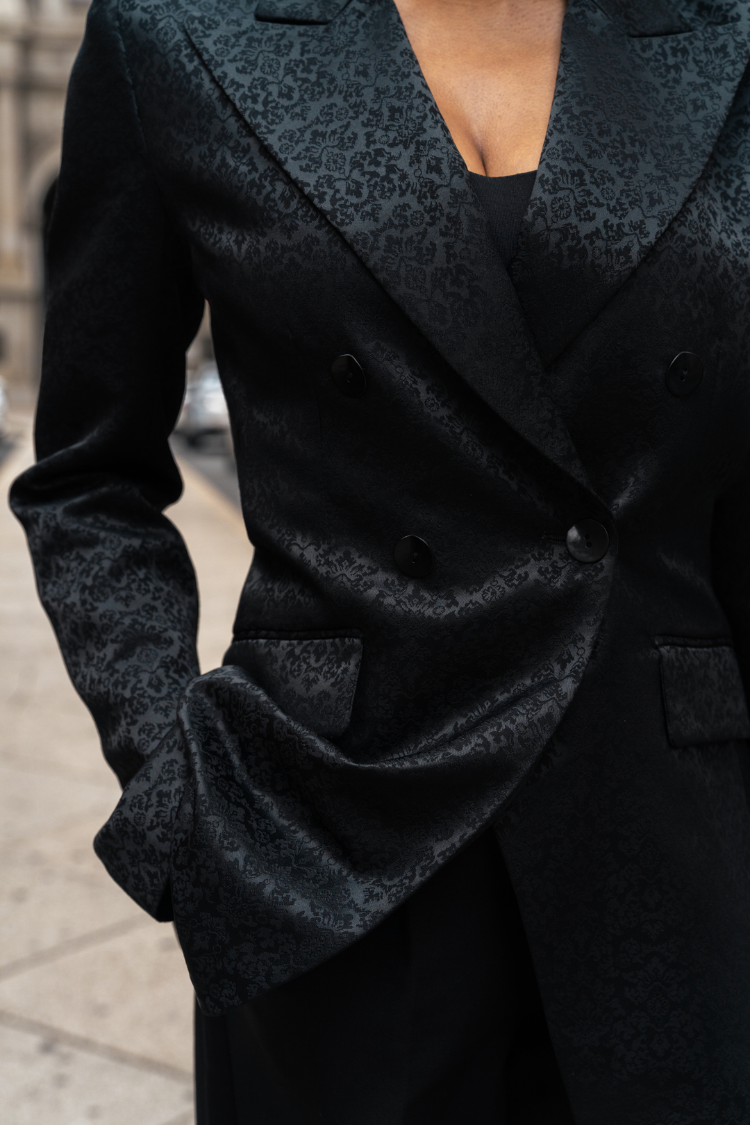 Black blazer double-breasted front detail: overlapping panels with dark buttons and pocket
