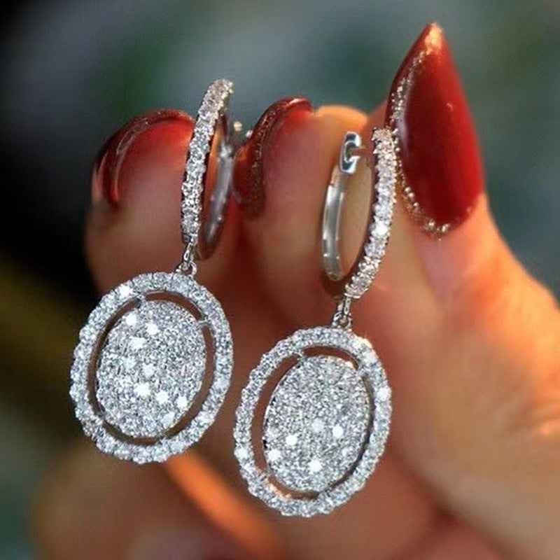 Oval drop earrings in white gold tone, pavé-style halo around the center oval stones