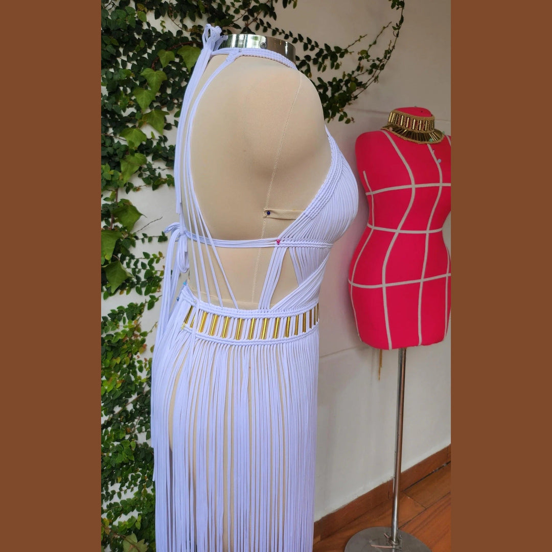 Selene ivory dress on mannequin: open-back crisscross straps, gold-accent waist, fringe maxi