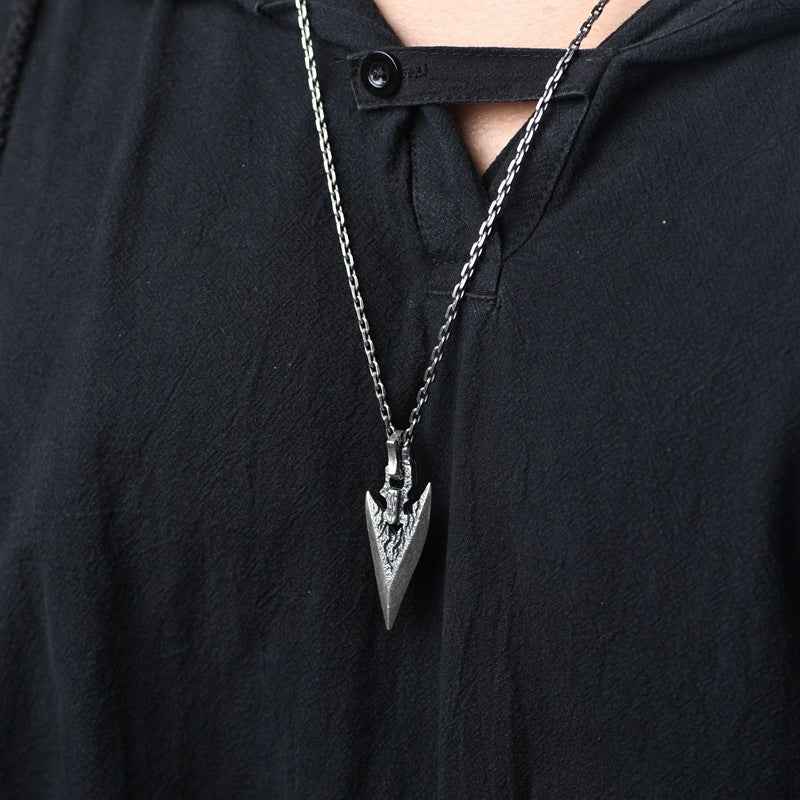 Silver weapon-shaped dagger pendant necklace worn at chest on dark shirt