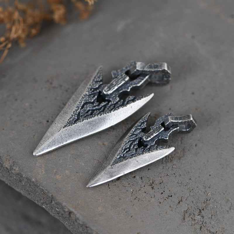 Two silver weapon-shaped dagger pendants, side-by-side showing dark engraved areas