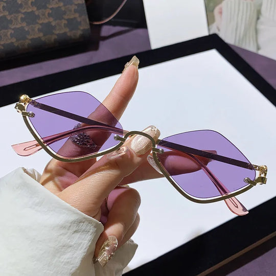 Hand hält Cat-Eye Sonnenbrille, goldfarbener Rahmen, violett getönte Gläser