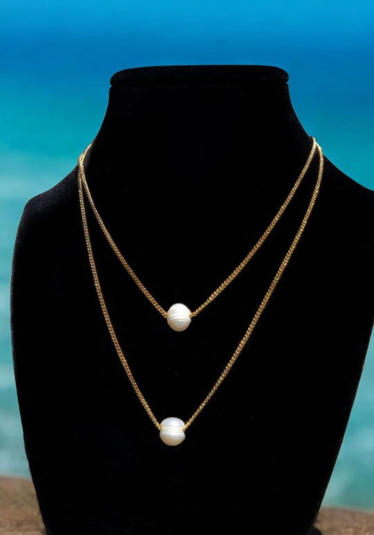 Layered gold curb chain necklaces with white freshwater pearl drops on mannequin