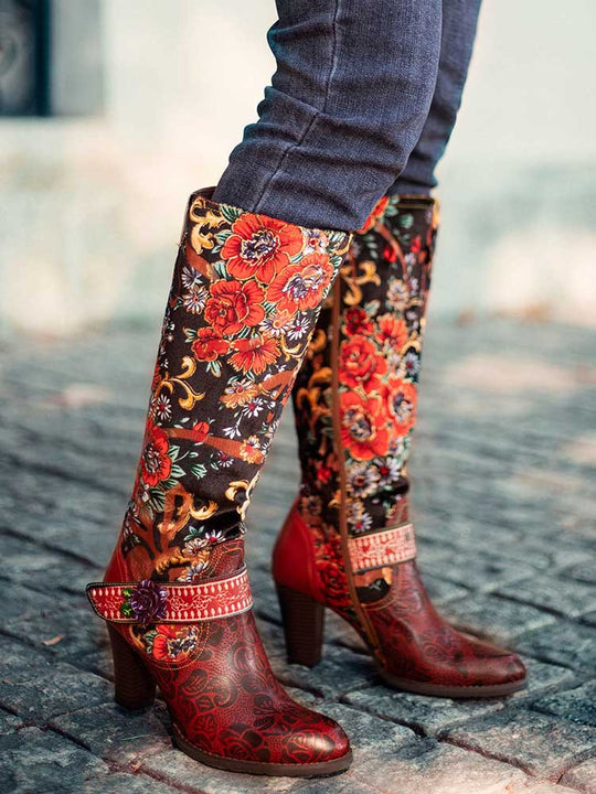 Floral embroidered boots with tall black shaft, red heel, and rounded toe on stone path
