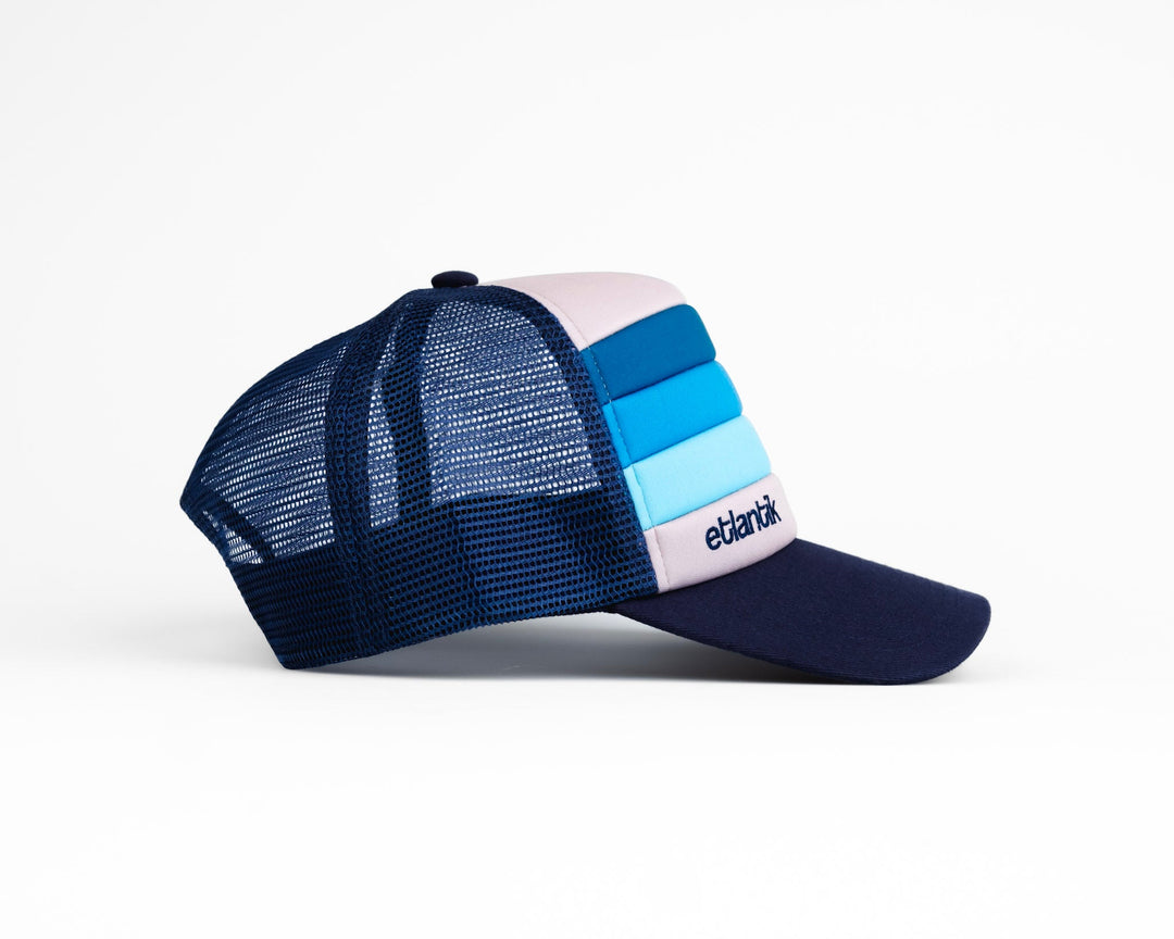 Swell Cap Blue: navy trucker cap with light-blue stripes, mesh back, and logo patch.