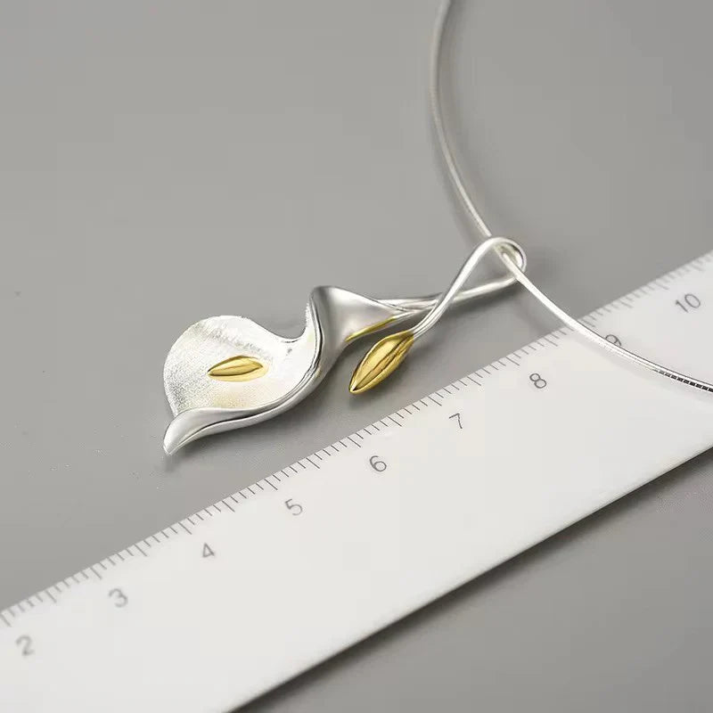 Silver calla lily necklace pendant with gold center, shown with a measurement ruler