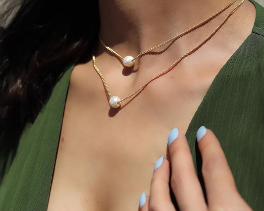 Layered gold curb chain necklaces with white freshwater pearls at neckline