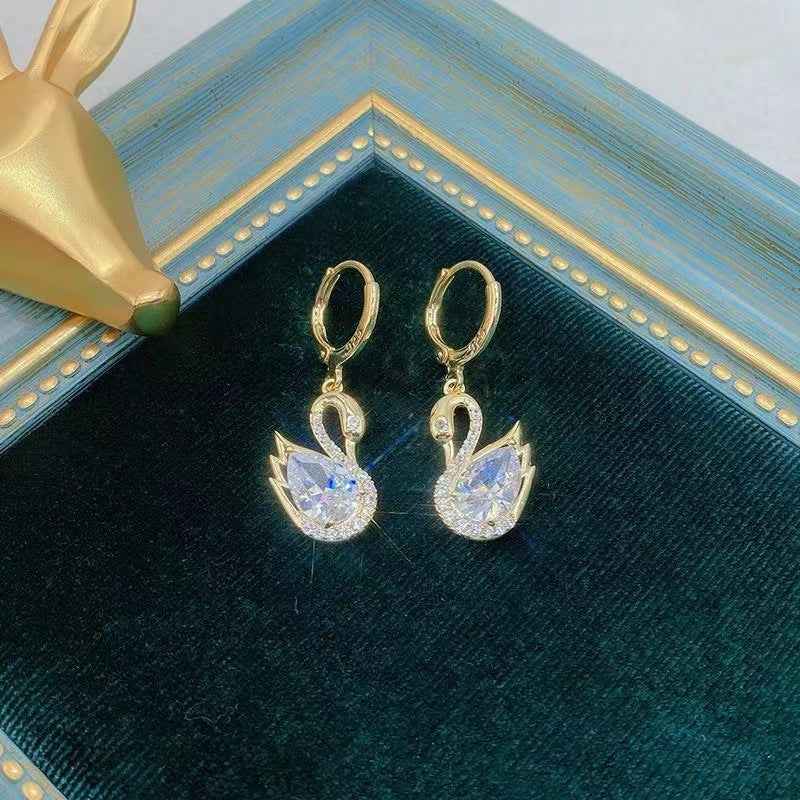 Gold-tone swan rhinestone drop earrings with circular hoops and clear faceted stones.