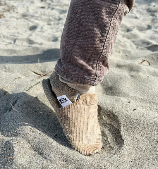 Beige corduroy moccasin slippers on sand, one shoe visible