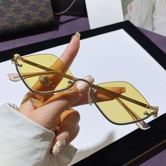 Hand hält Cat-Eye Sonnenbrille, goldfarbener Metallrahmen, gelb getönte Gläser