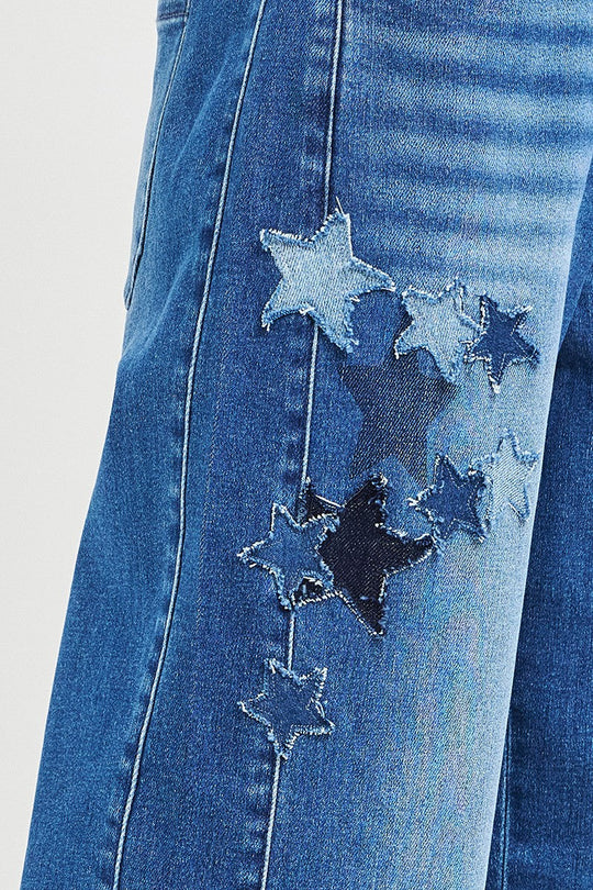 Close-up of dark denim star patches with stitched edges on cropped jeans