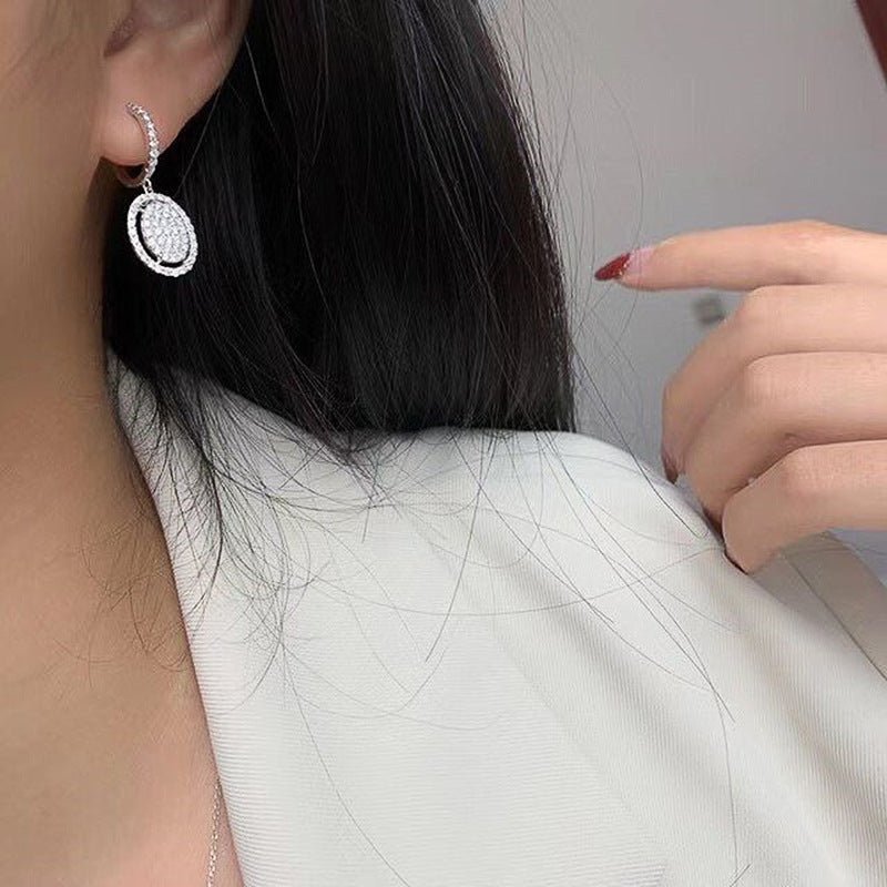 White gold oval drop earring with pavé halo, shown from the side on the ear