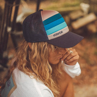 Swell Cap Blue on head: navy trucker cap with light-blue striped front panel.