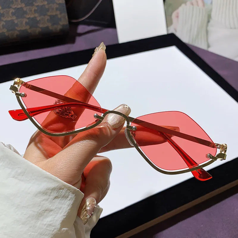 Hand hält Cat-Eye Sonnenbrille mit roten getönten Gläsern und goldfarbenen Akzenten