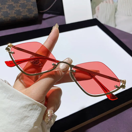 Hand hält Cat-Eye Sonnenbrille mit roten getönten Gläsern und goldfarbenen Akzenten