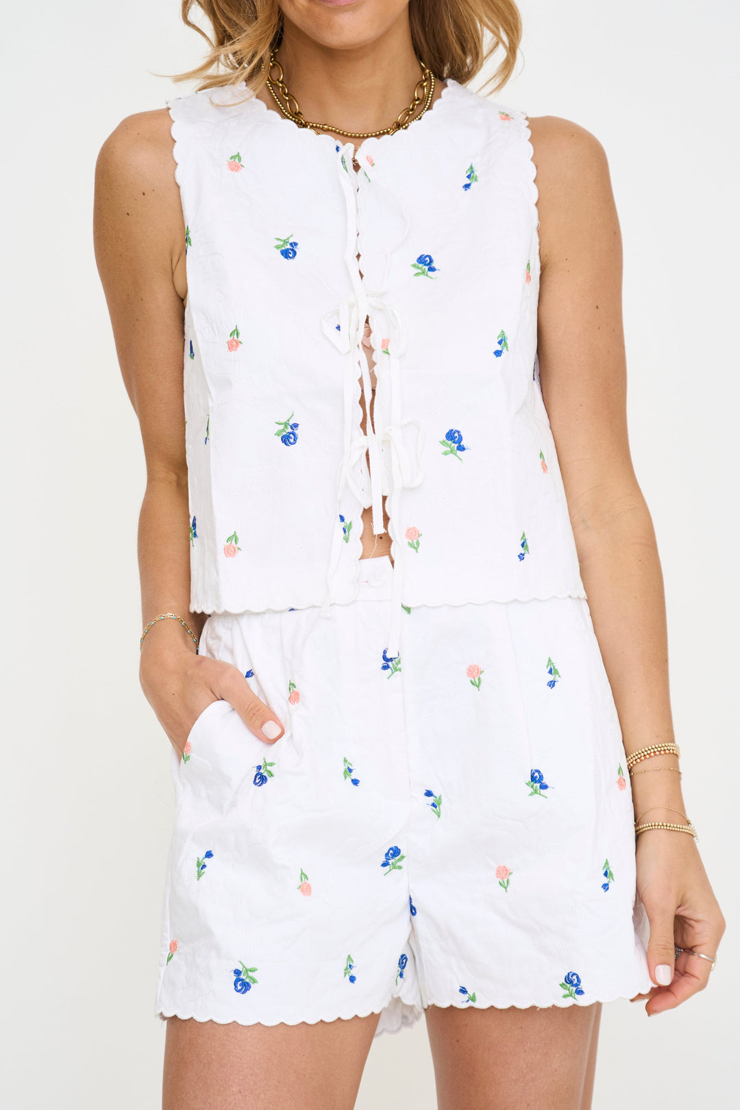 Chaleco blanco con estampado floral azul y rosa y cordón con borlas; set con shorts