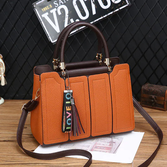 Orange shoulder tote with brown handles, gold hardware, tassel charm hanging from center panel
