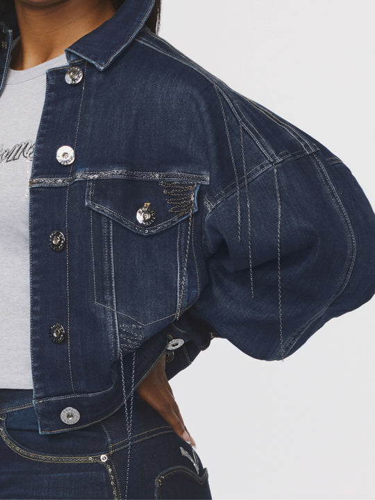 Blue denim jacket sleeve and chest pocket detail with snap buttons and stitching