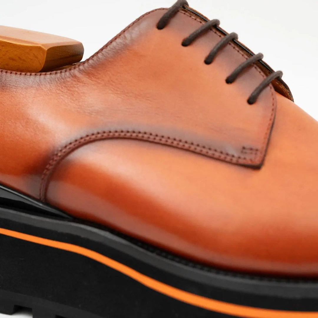 Brown derby shoe upper close-up with lace, stitched seam, and orange edge trim