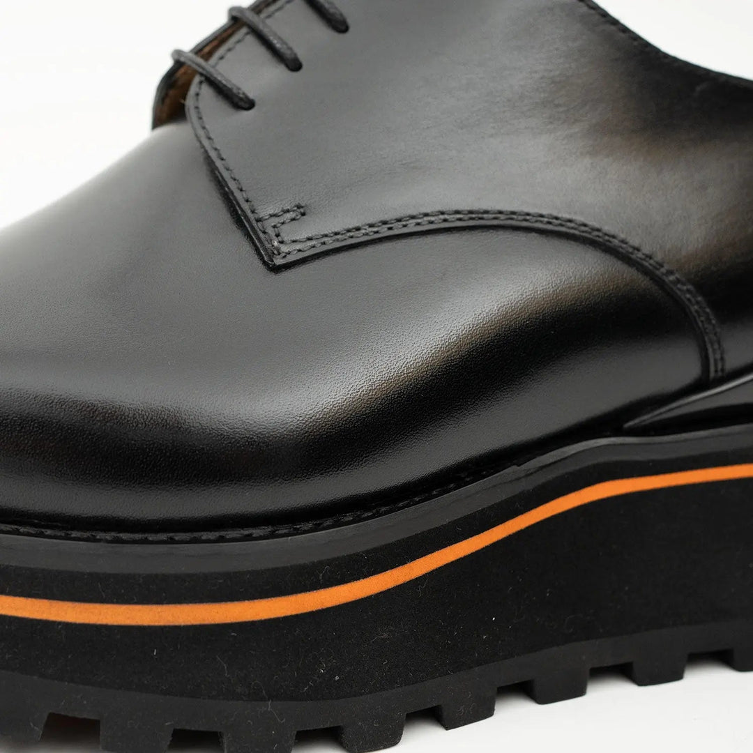 Close-up of black leather derby shoe: orange welt stripe and textured rubber sole