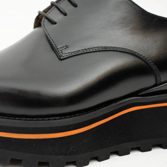 Close-up of black leather derby shoe: orange welt stripe and textured rubber sole