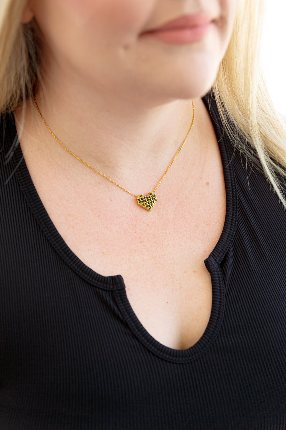 Gold-tone checkered heart necklace on collarbone, pendant centered on thin chain