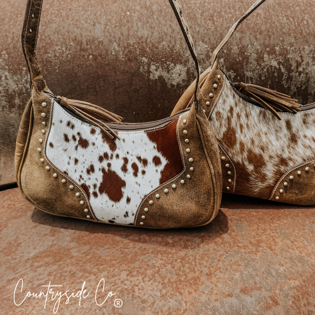 Side view of cowhide leather handbag with white-and-brown hide panels and studded edge