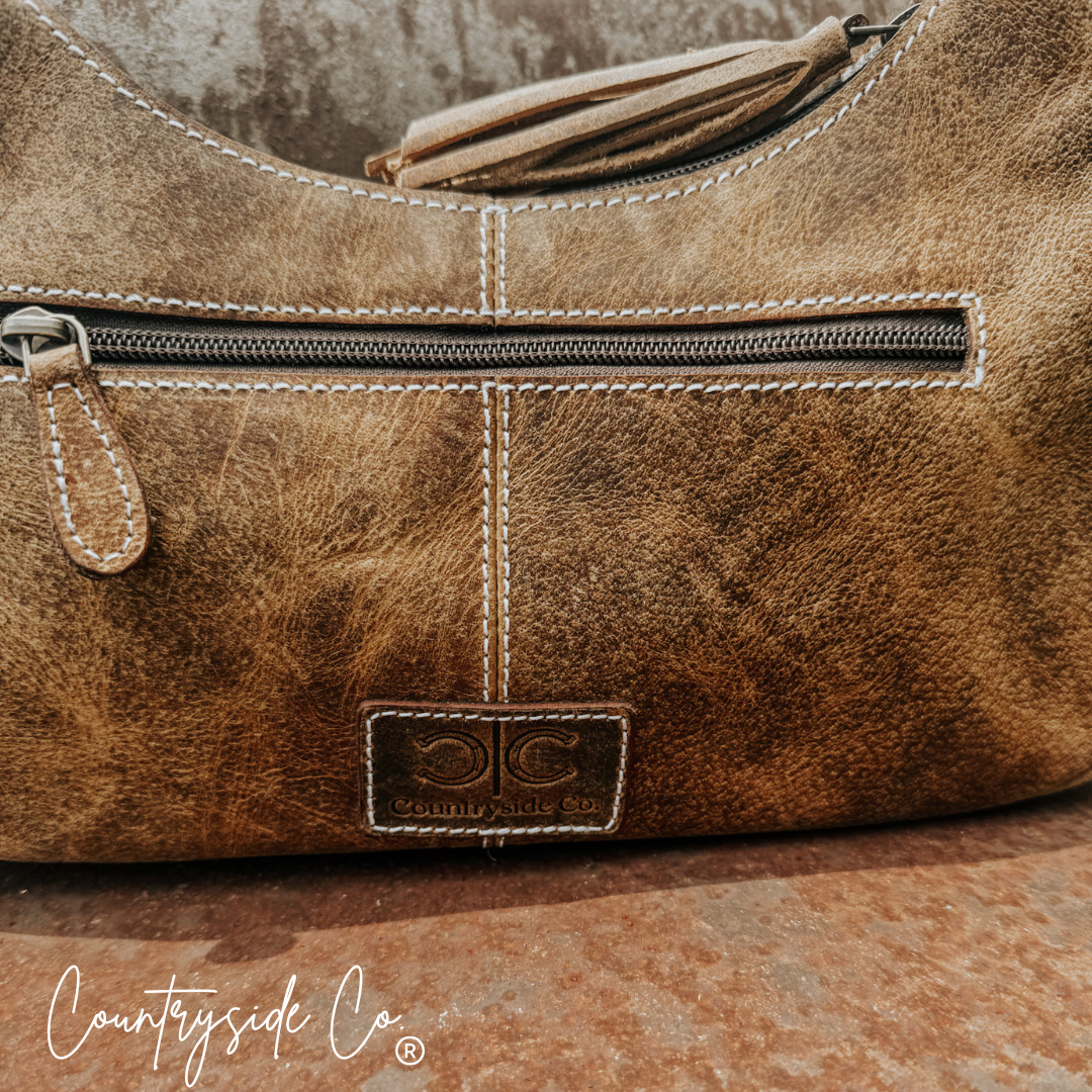 Cowhide leather handbag close-up: top zipper, stitched panels, Countryside Co. patch logo