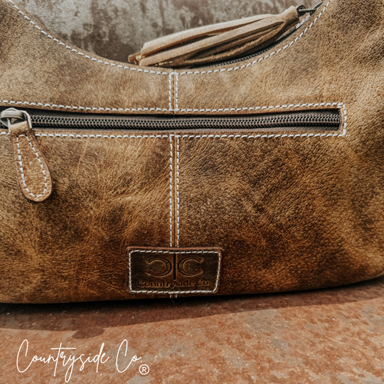 Cowhide leather handbag close-up: top zipper, stitched panels, Countryside Co. patch logo