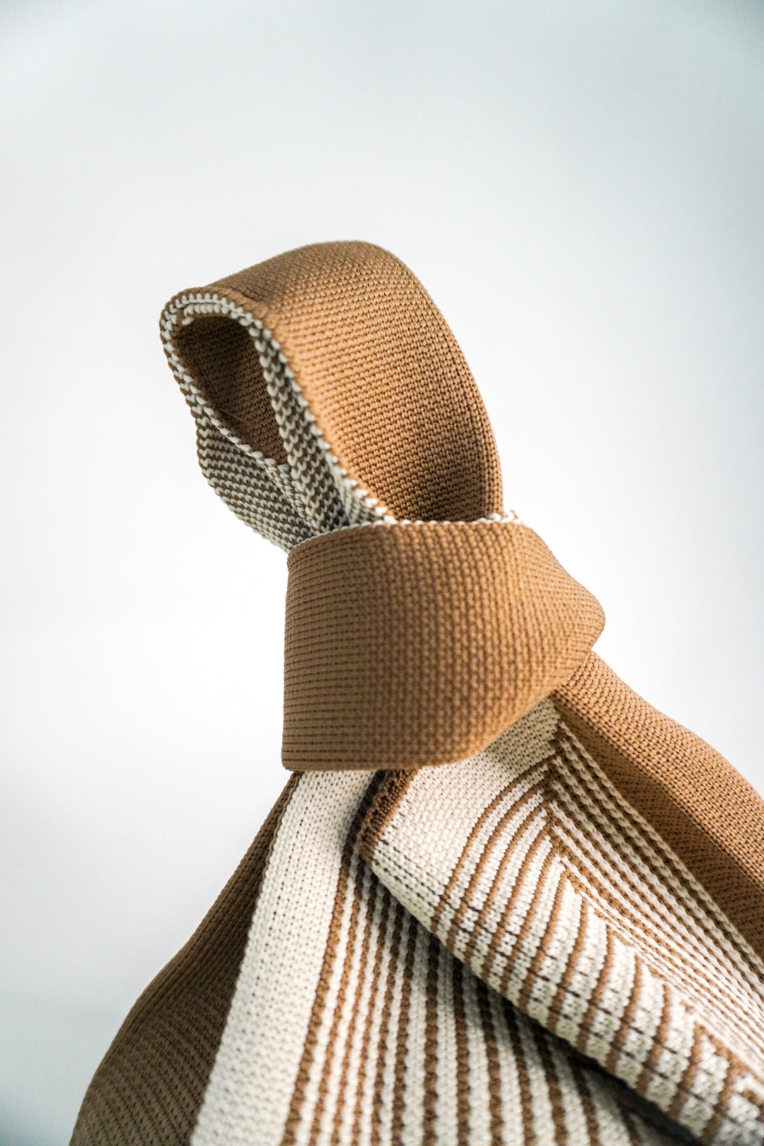 Beige twisted handle and woven labyrinth stripe pattern on bag body