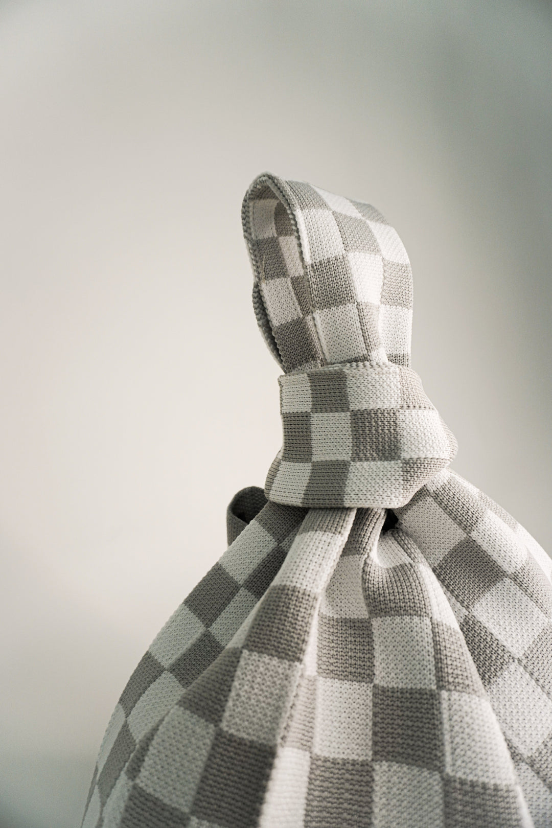Top view of grey-and-white checkered drawstring bag, fabric knot detail