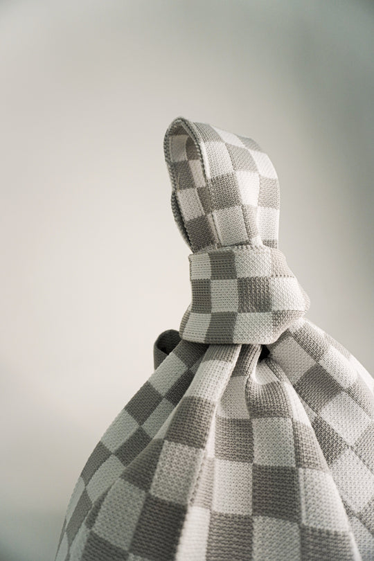 Top view of grey-and-white checkered drawstring bag, fabric knot detail