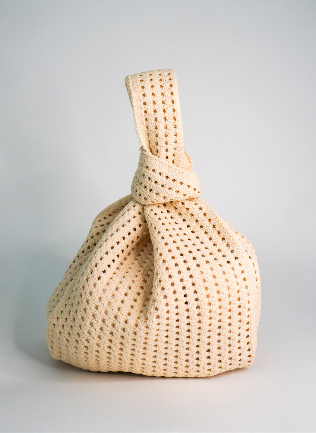 Oat crochet drawstring handbag with twisted top tie and openwork stitch texture.