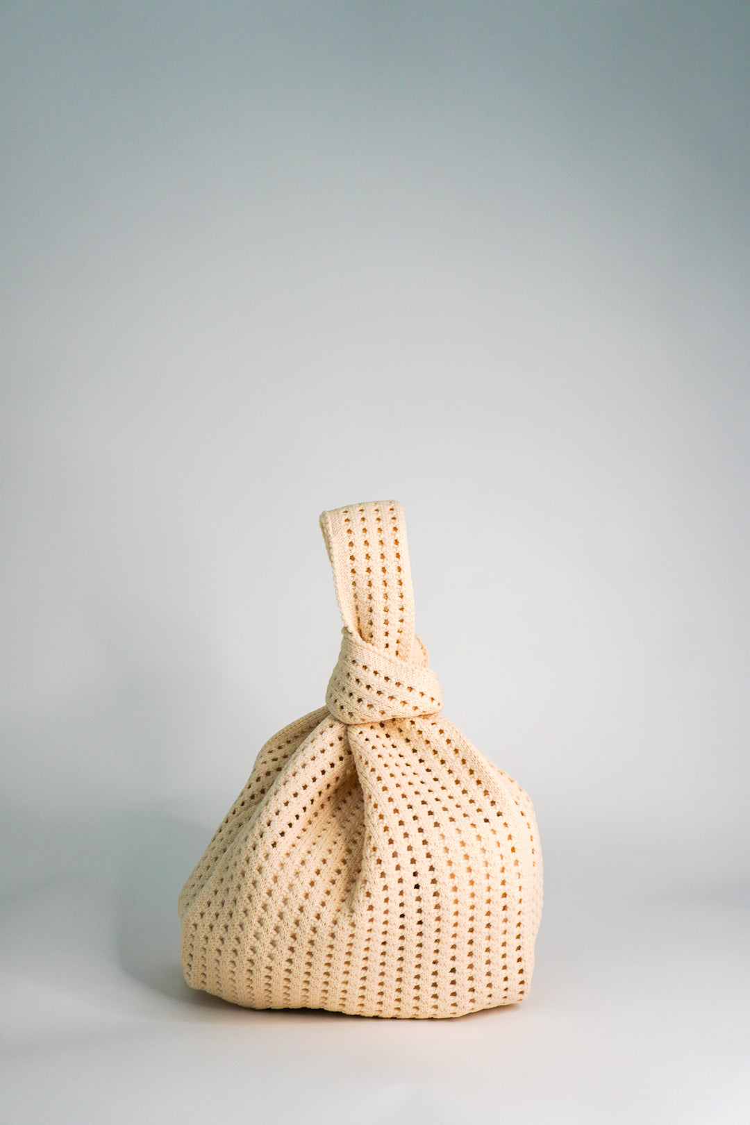 Oat crochet drawstring handbag with rounded body and gathered top tied into a long bow.