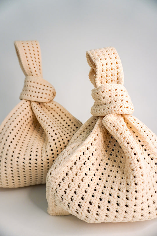 Two oat crochet drawstring handbags with knotted ties and openwork lattice stitch pattern.