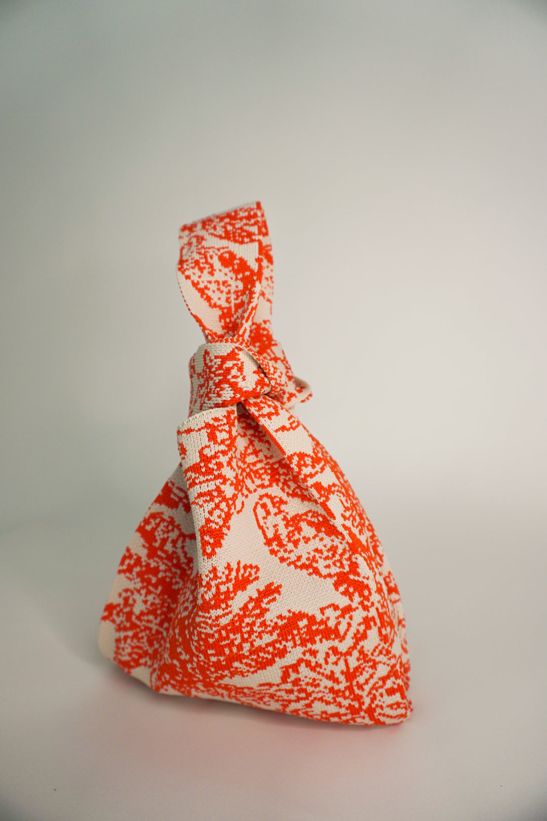 Orange and cream patterned pouch handbag with twisted handle and compact shape