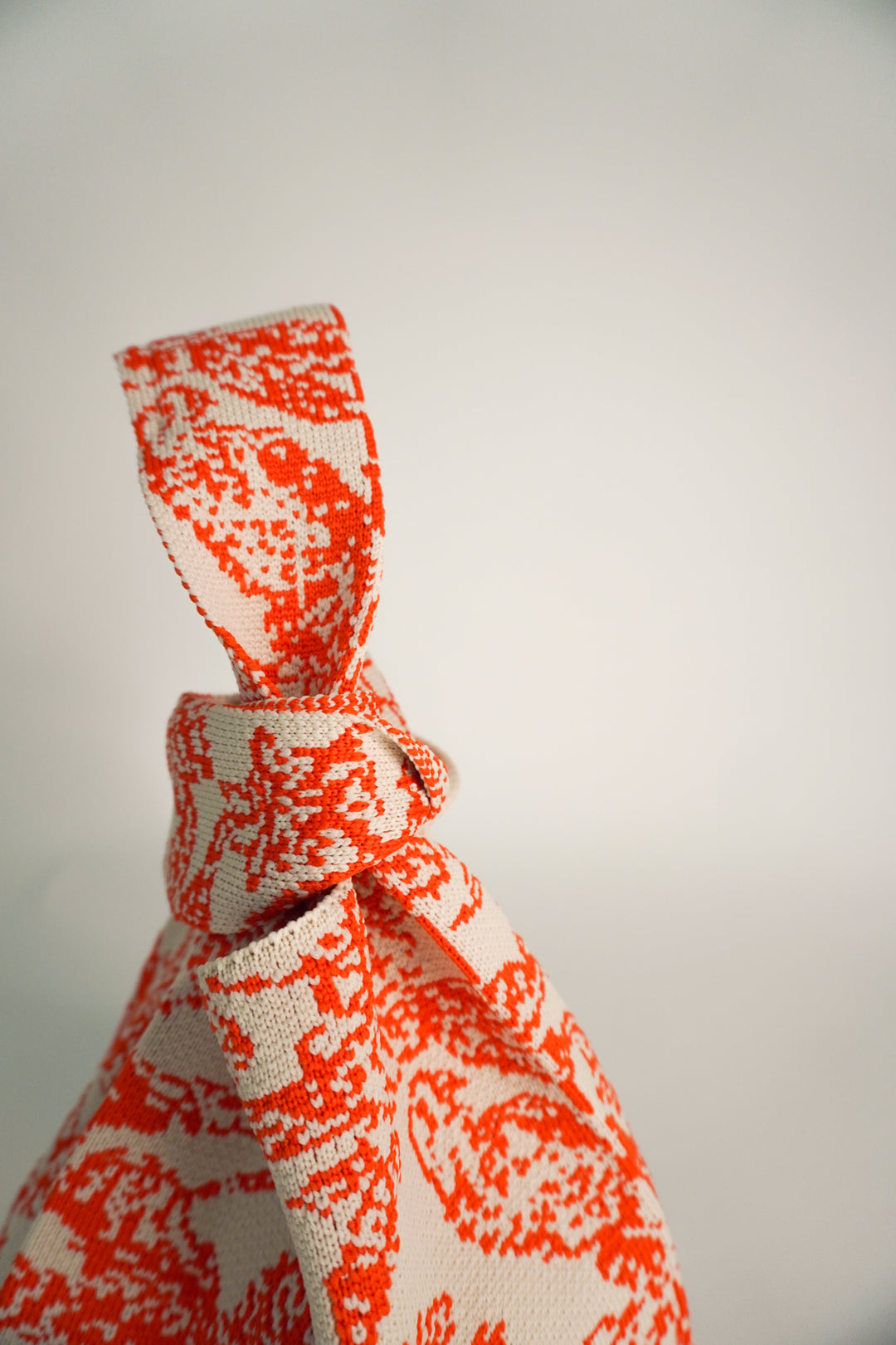 Orange and cream patterned pouch handbag with tied knot strap and rounded base