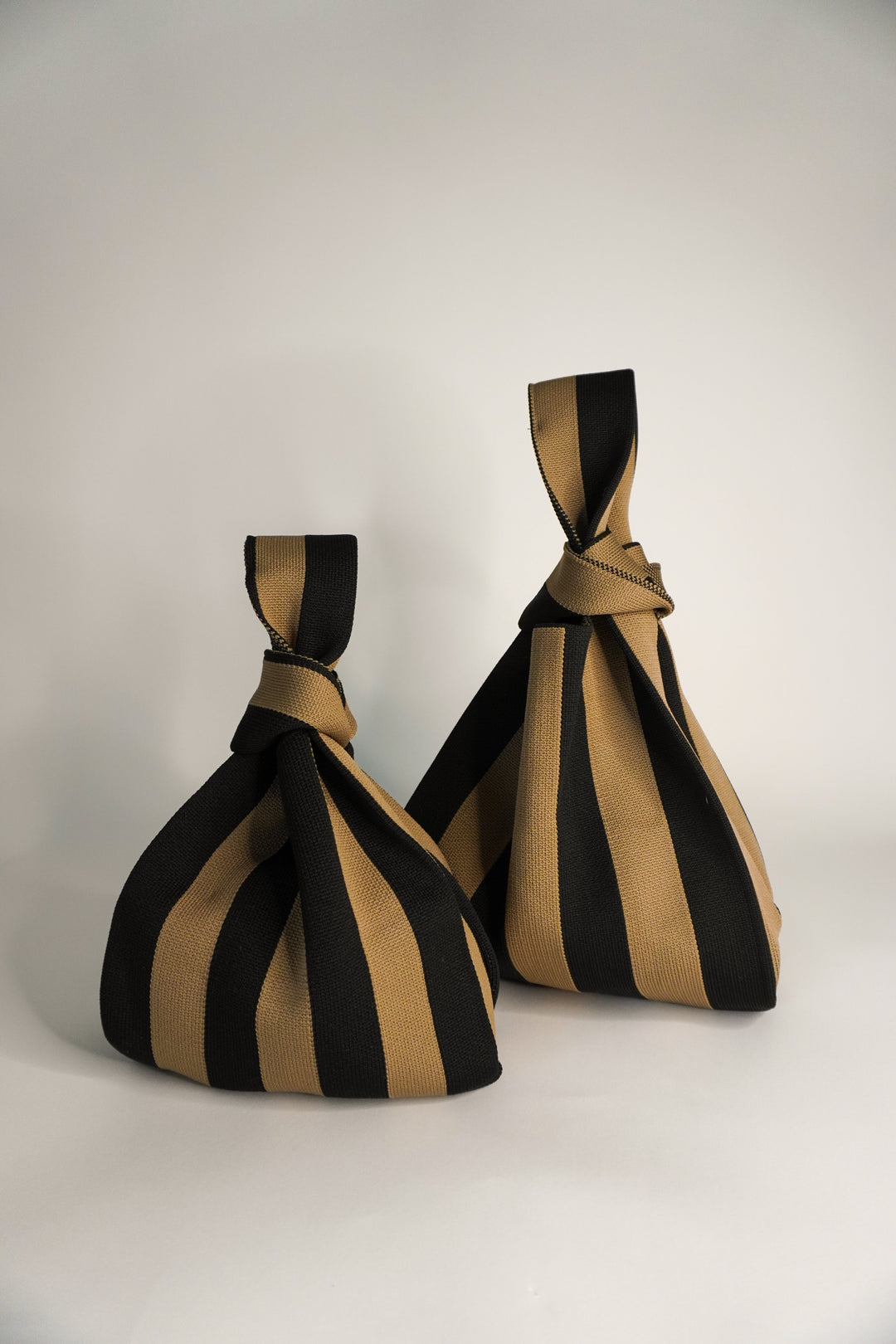 Dos bolsos con rayas negro y marrón y la parte superior anudada tipo lazo, diseño tipo saco