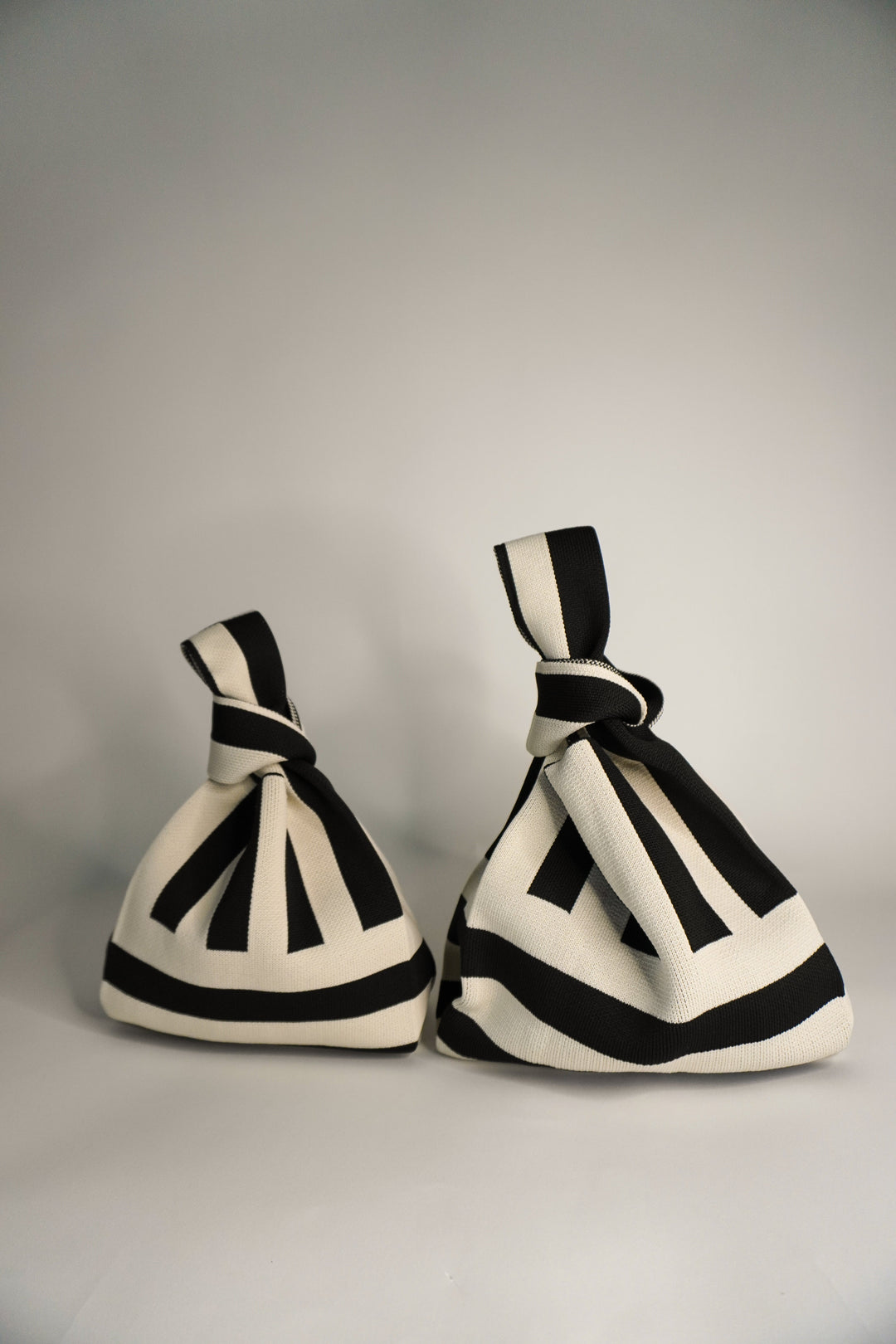 Two The Original² black-and-cream striped drawstring handbags, side view