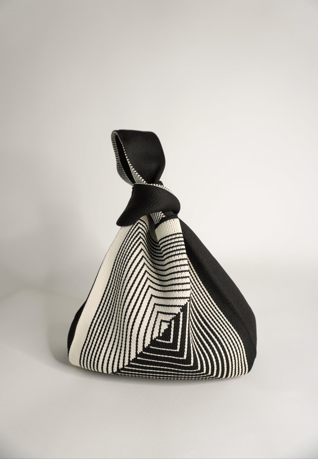 Black hand bag pouch with geometric labyrinth stripes and knotted top handle.