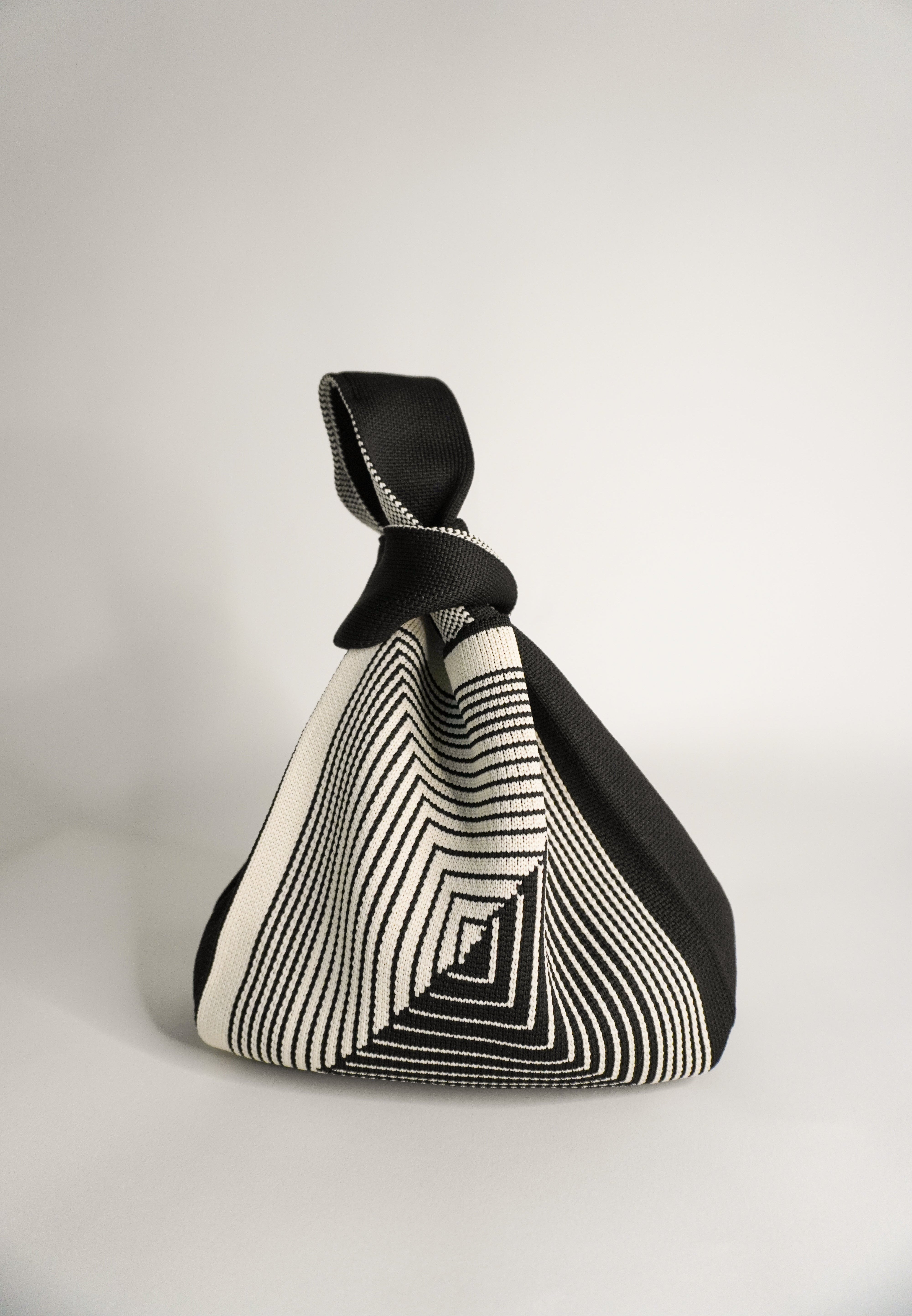 Black hand bag pouch with geometric labyrinth stripes and knotted top handle.