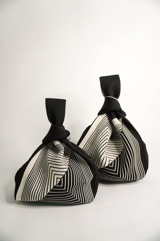 Two black drawstring pouch bags with cream labyrinth stripe panels and knotted tops.