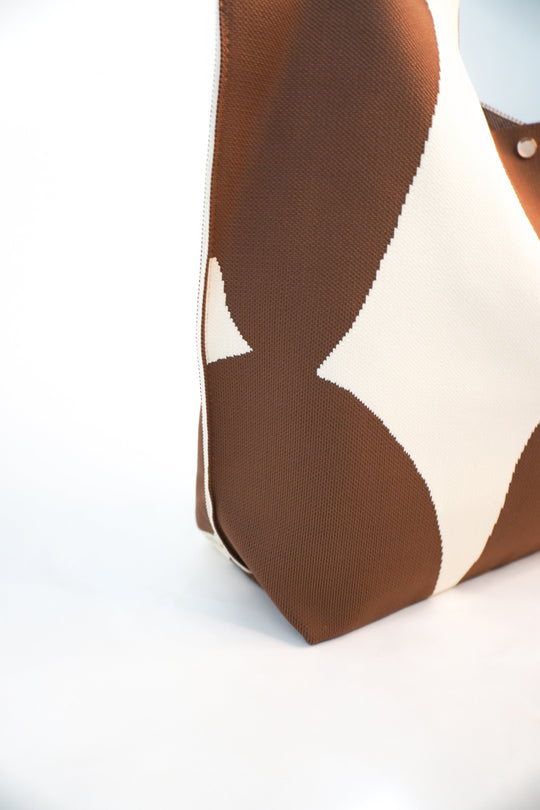 Close-up of brown tote corner with cream abstract shape and visible woven texture