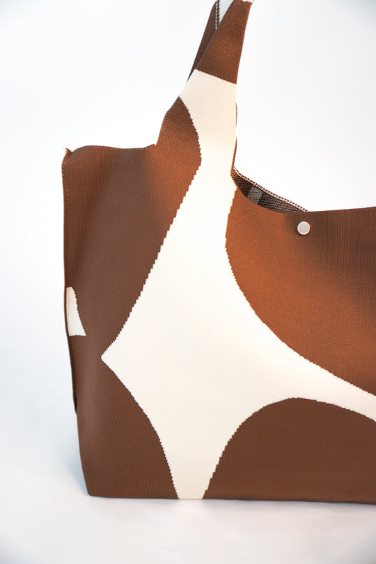Brown tote with cream abstract patches, textured fabric, top edge with metal grommet