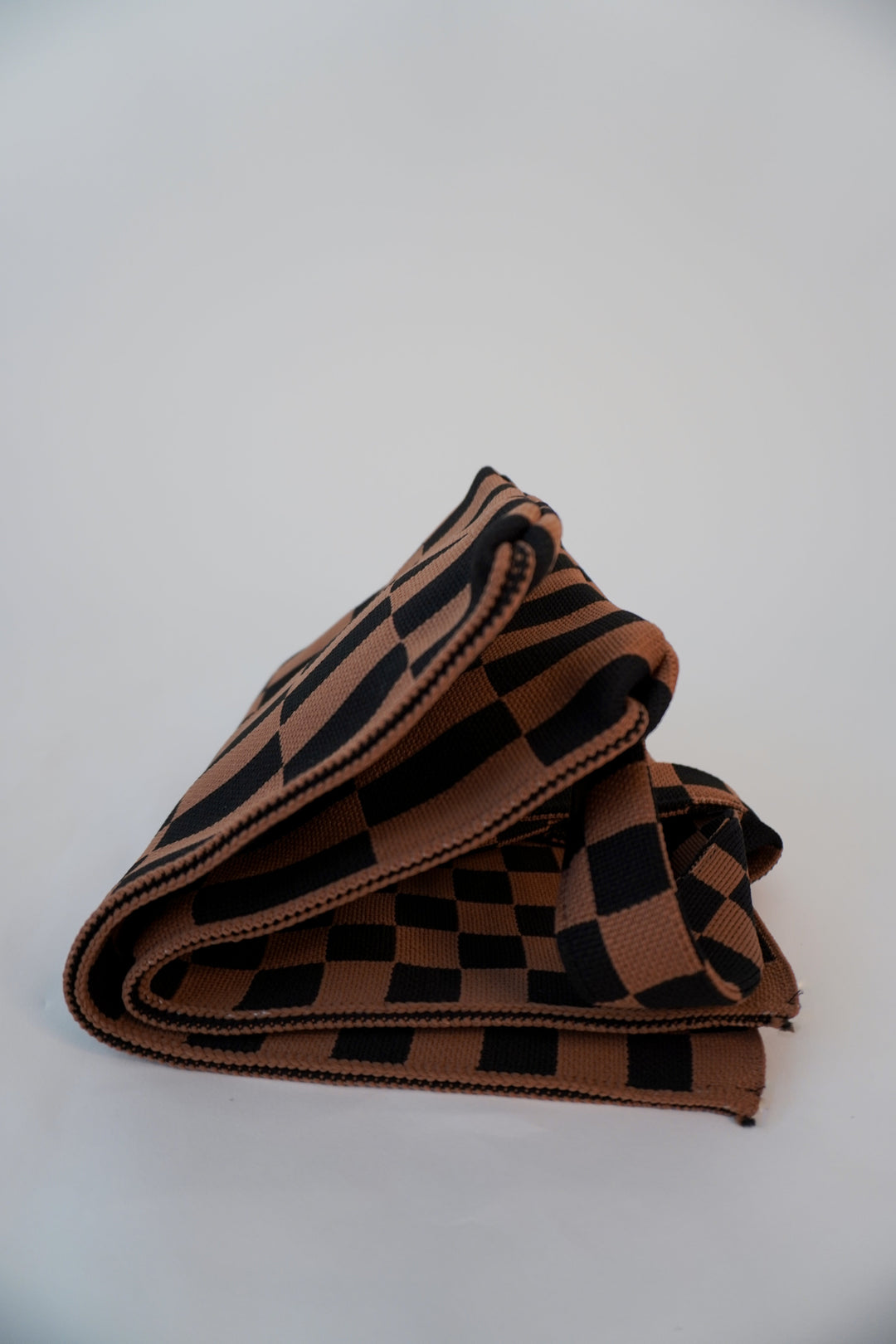 Folded checkered skinny tote with stacked stripes and brown-and-black square pattern.